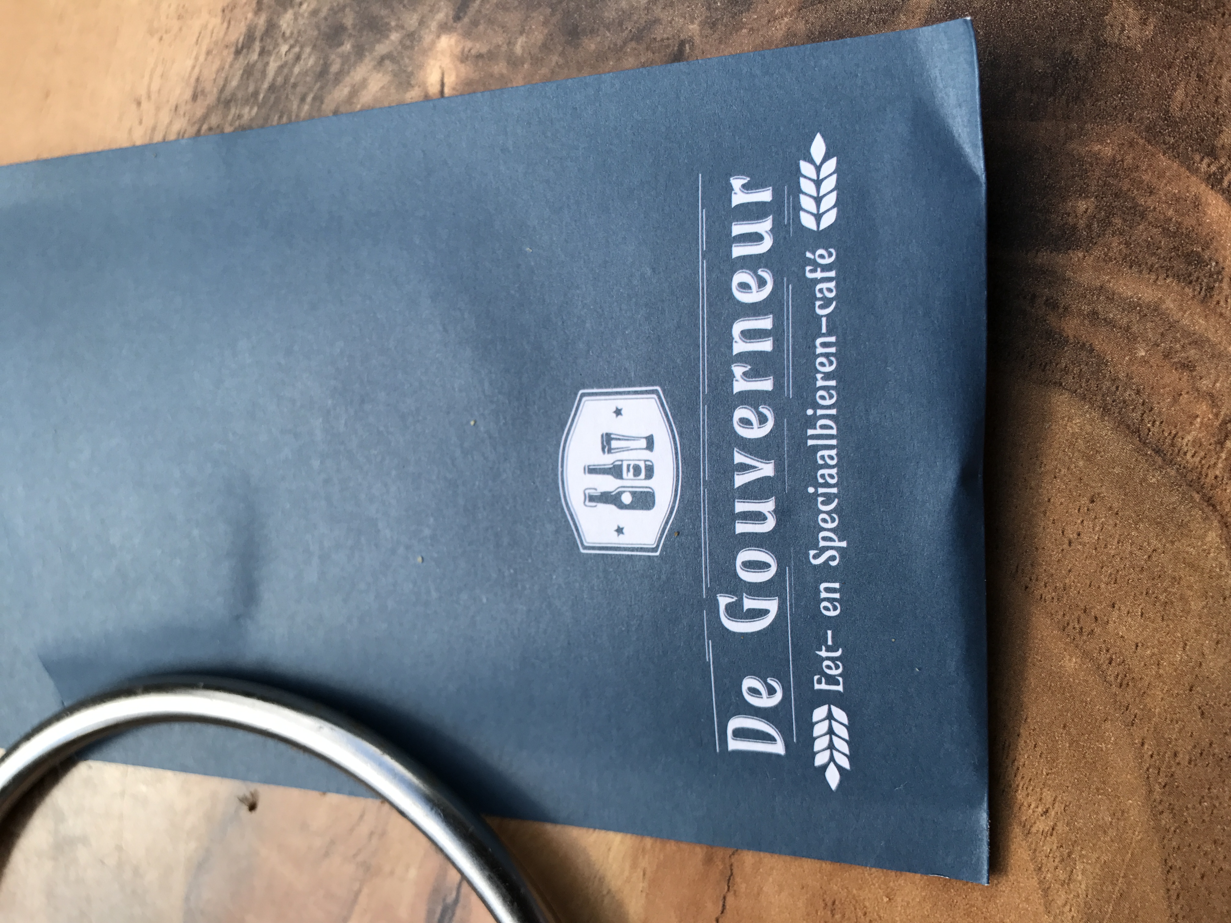 Granatowa serwetka De Gouverneur Eet- en Speciaalbieren-café na drewnianym stoliku w Maastricht.