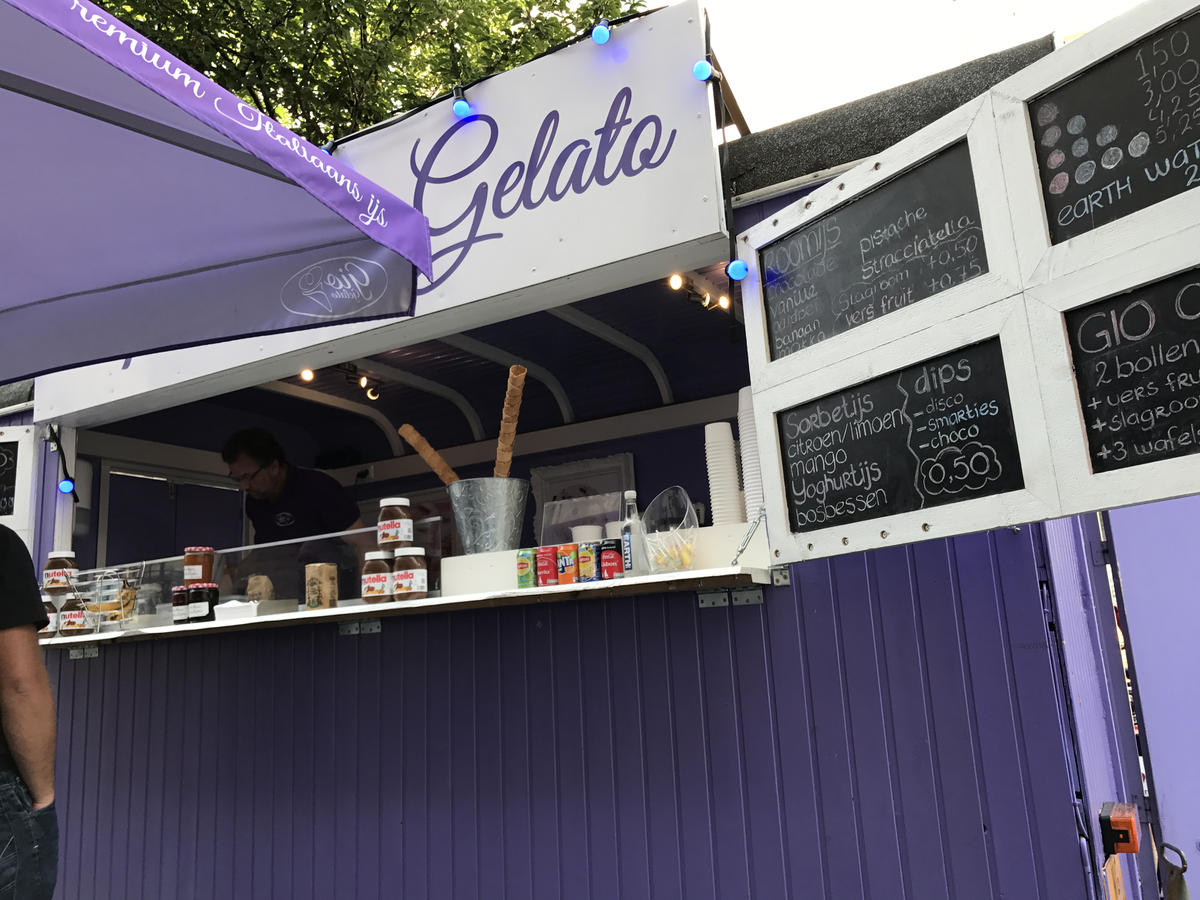 Fioletowa budka z napisem Gelato na targu w Maastricht, serwująca lody i naleśniki.