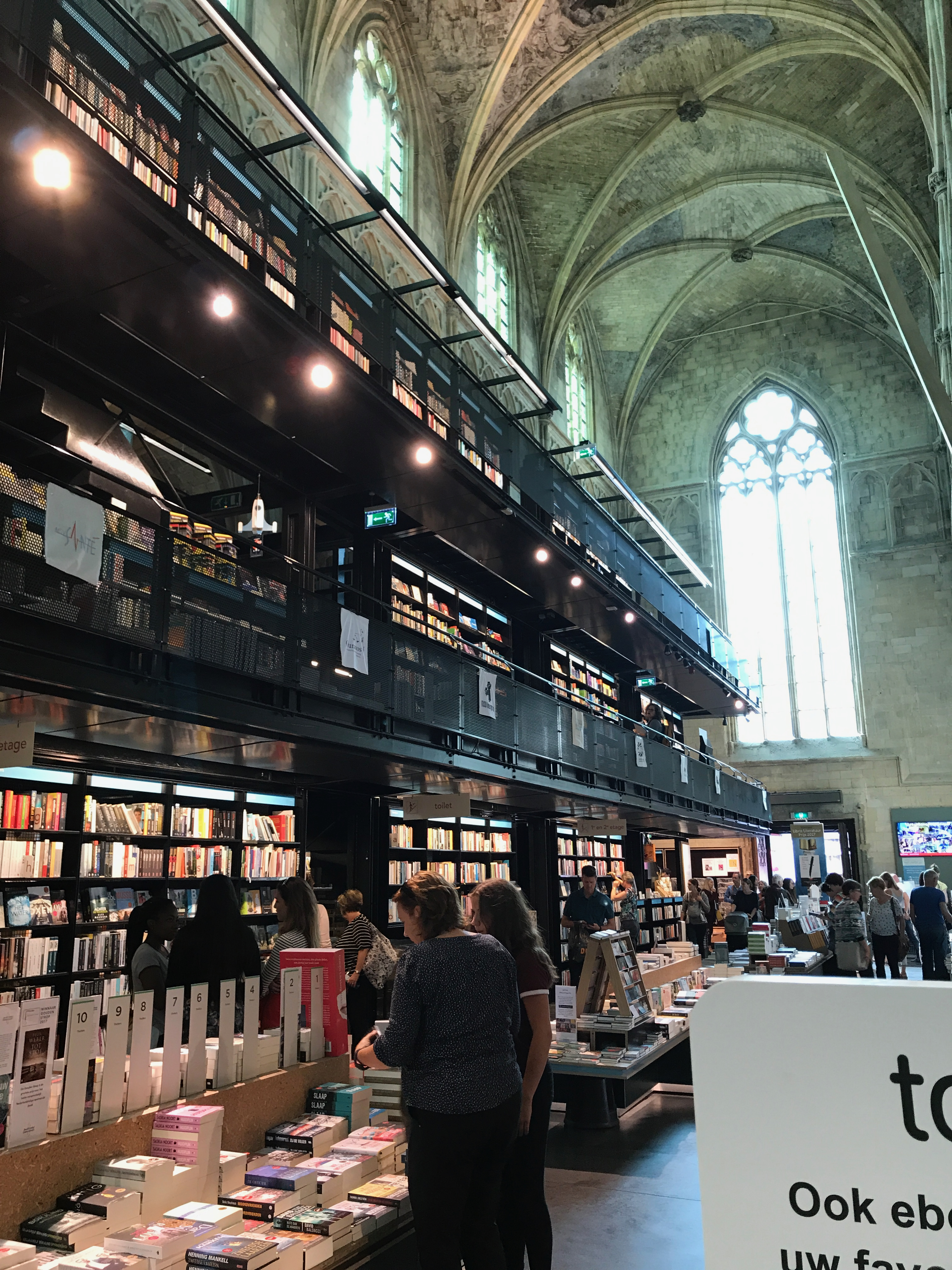 Regały i kawiarnia we wnętrzu Boekhandel Dominicanen w Maastricht, pod wysokimi gotyckimi sklepieniami dawnego kościoła.