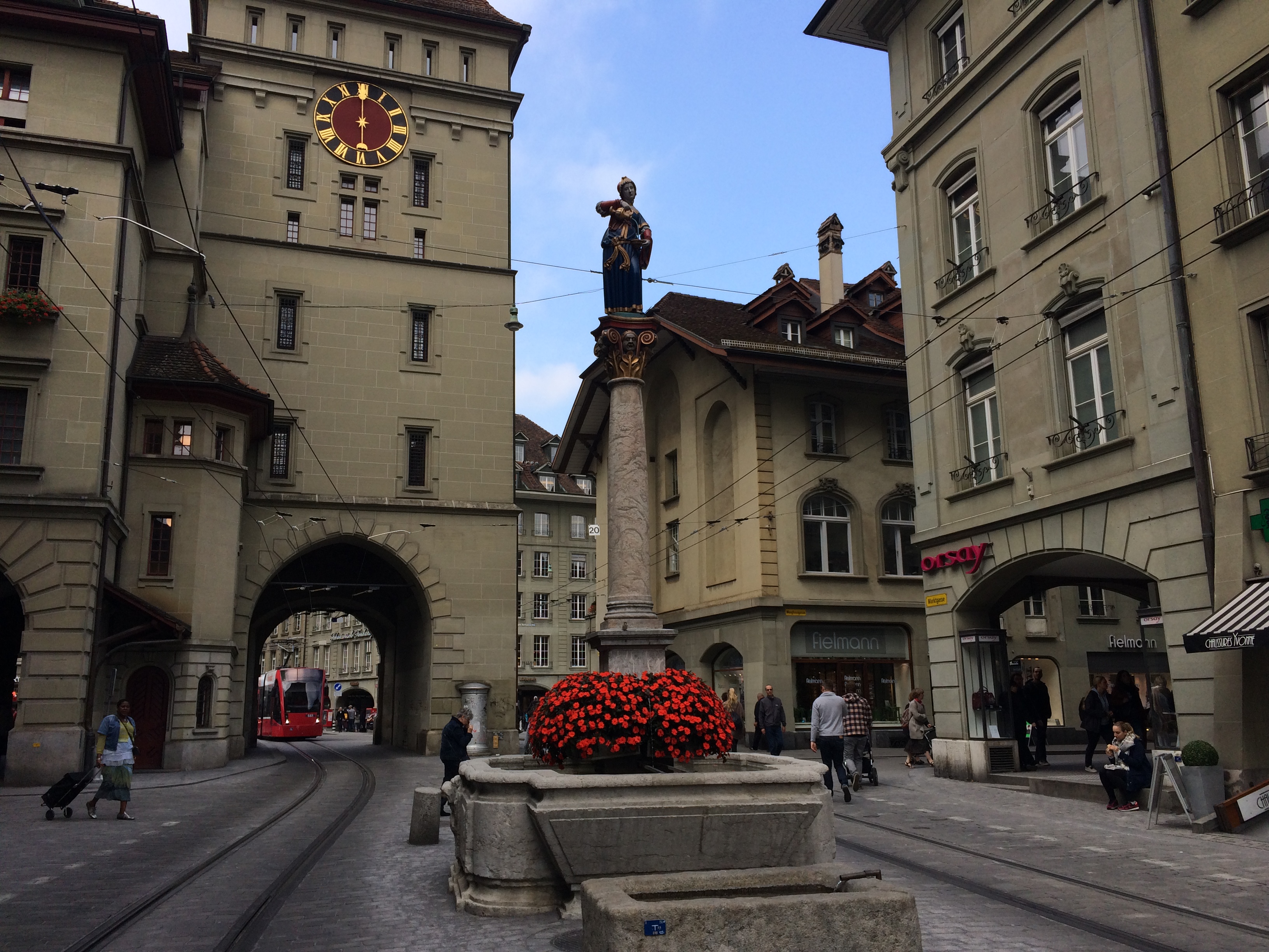 Zytglogge i Simsonbrunnen na starym mieście w Bernie, z tramwajem przejeżdżającym pod wieżą zegarową.