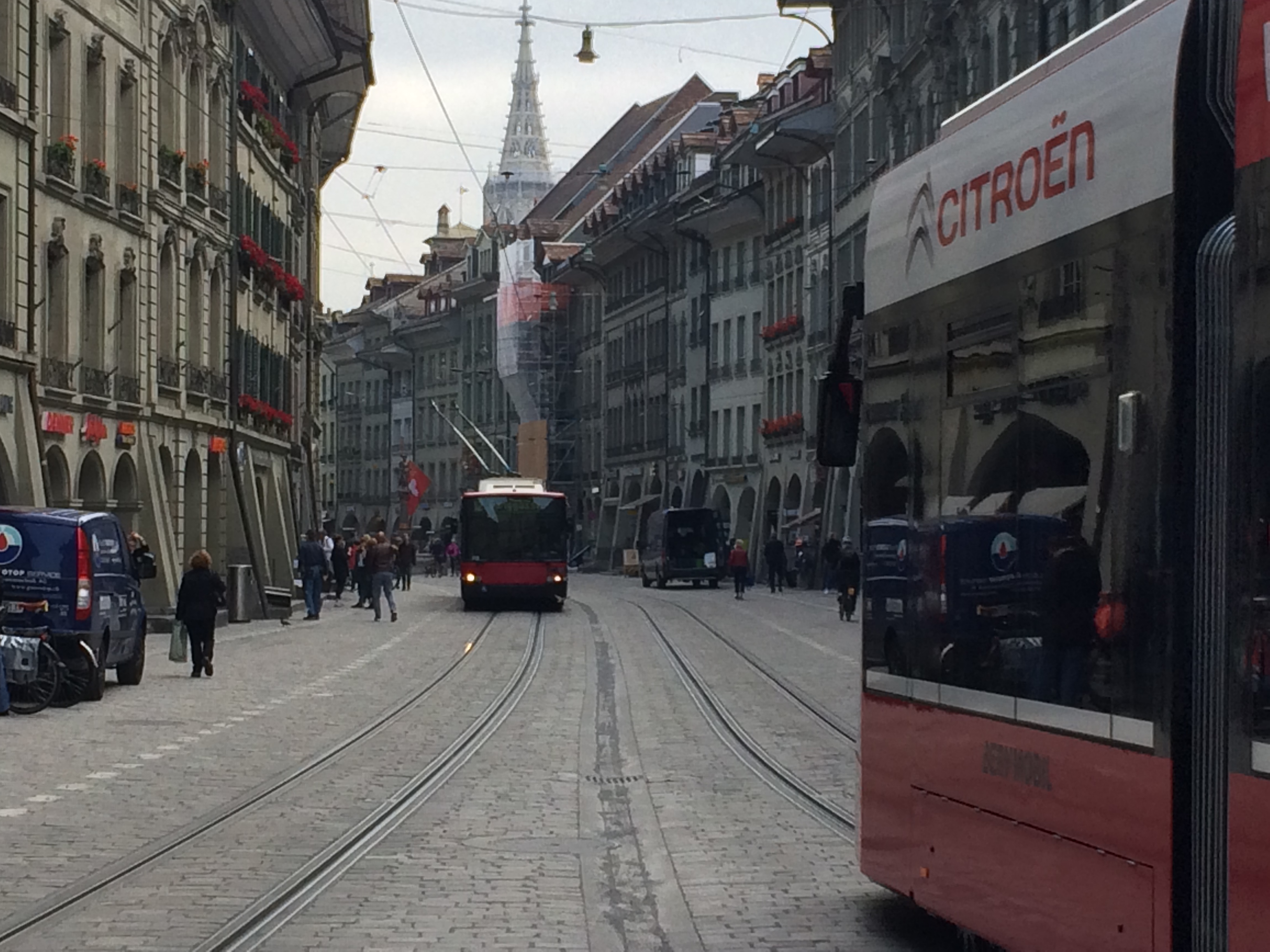 Ulica starego miasta w Bernie z tramwajami, torami, arkadami i wieżą Berner Münster w tle.