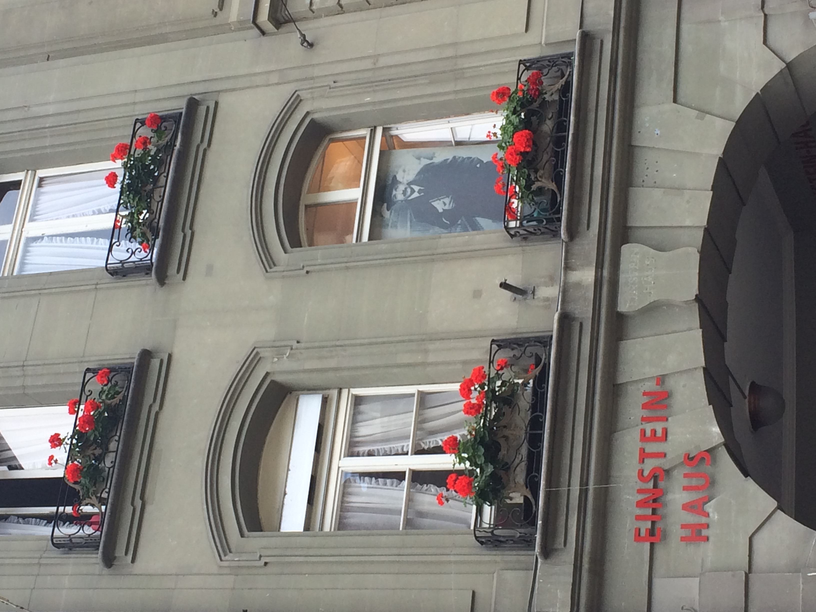 Einstein Haus w Bernie przy Kramgasse 49, z napisem Einstein-Haus, czerwonymi kwiatami w oknach i zdjęciem Alberta Einsteina.