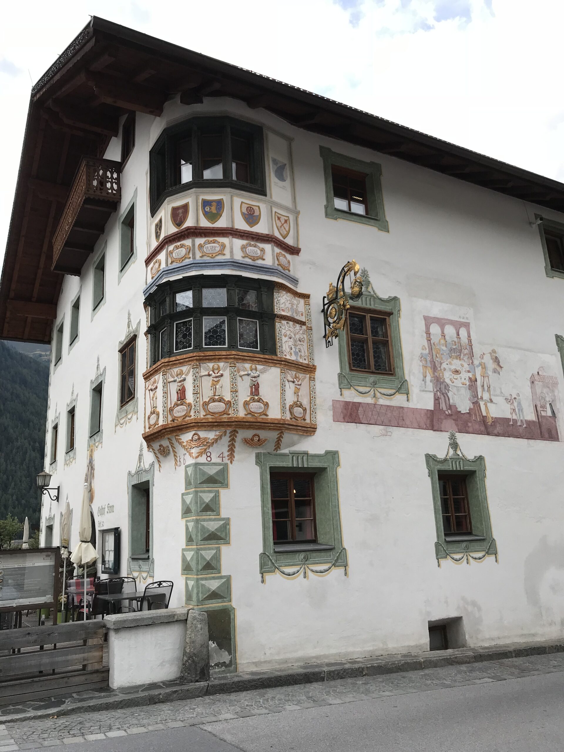 Zdobiona fasada starego budynku w Umhausen Zdobiona fasada starego budynku w Umhausen z malowanym wykuszem, herbami, scenami figuralnymi i górskim tłem.
