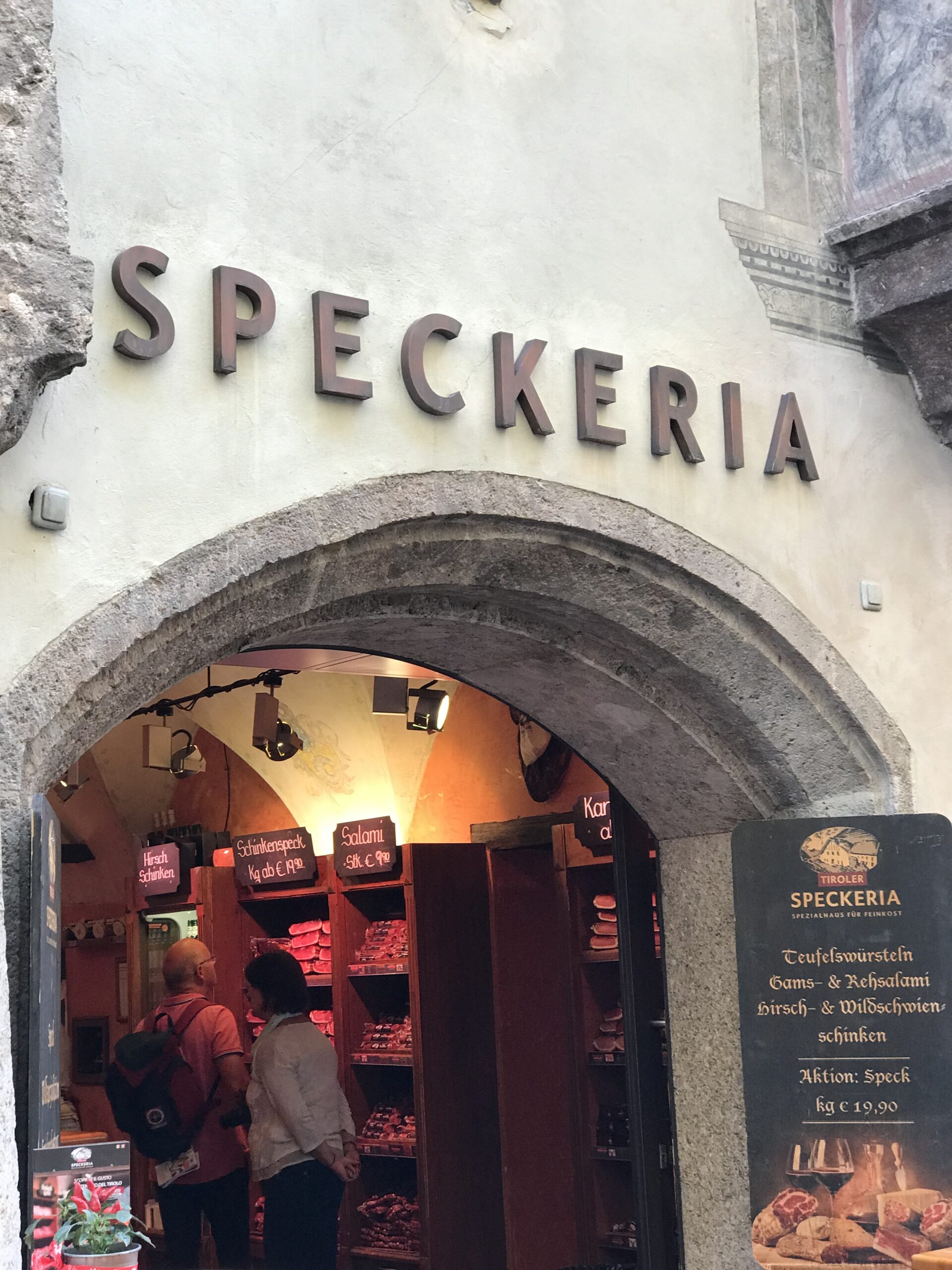 Wejście do Tiroler Speckeria w Innsbrucku Wejście do Tiroler Speckeria w Innsbrucku z półkami wędlin, szyldem i tablicą z lokalnymi specjalnościami
