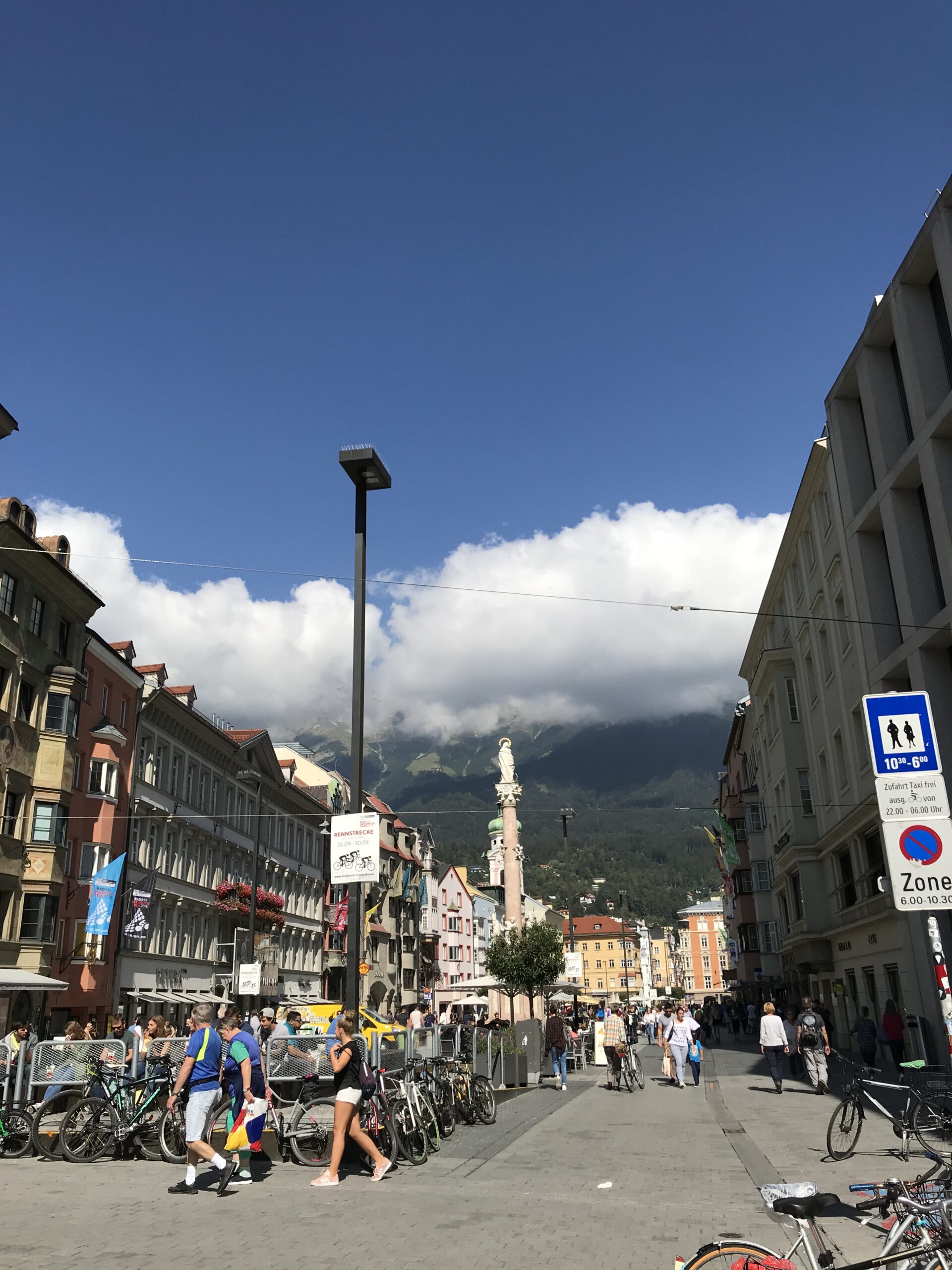 Maria-Theresien-Straße i Nordkette w Innsbrucku Maria-Theresien-Straße w Innsbrucku z Kolumną św. Anny, rowerami, spacerującymi ludźmi i chmurami nad górami Nordkette