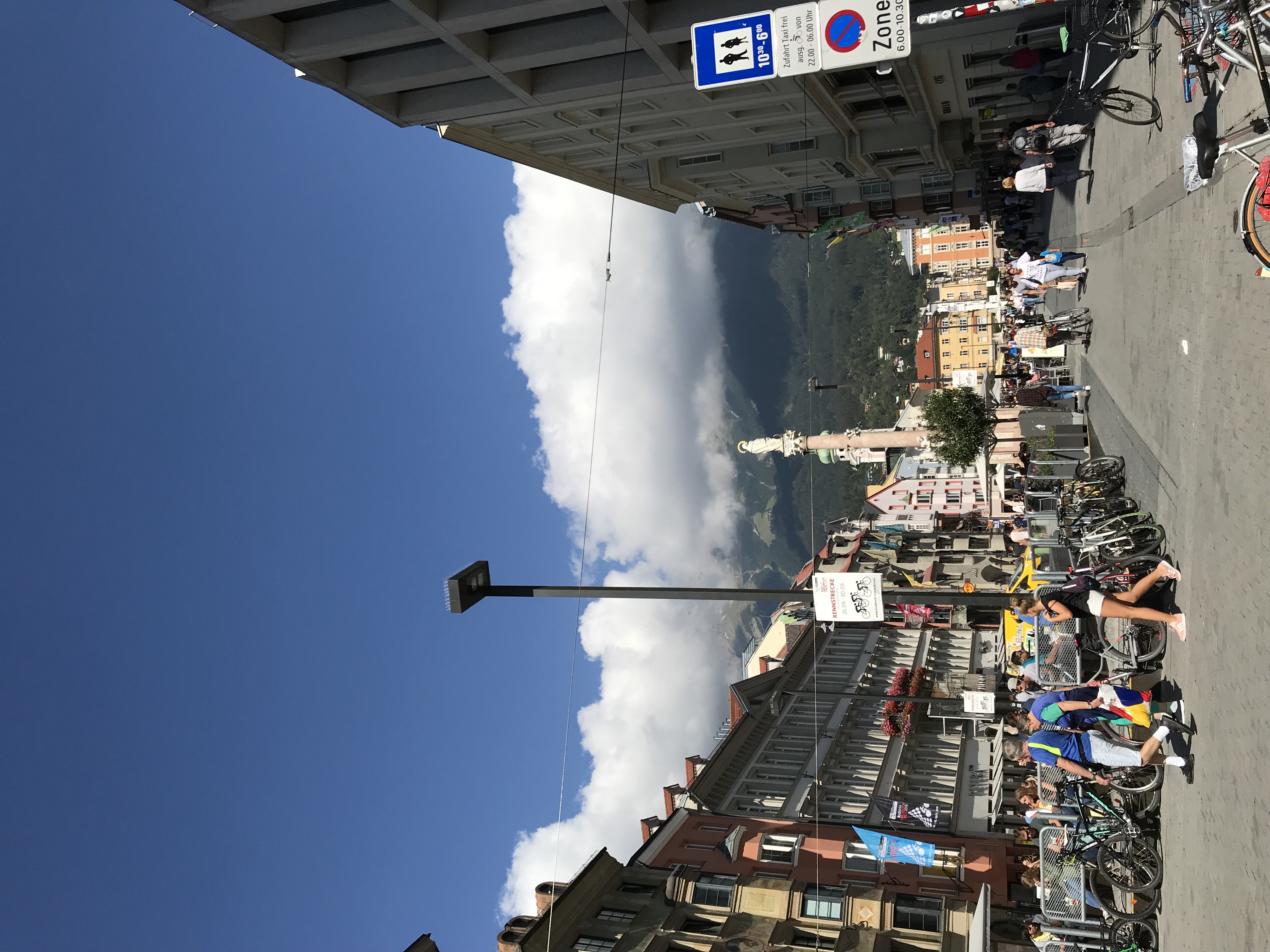 Maria-Theresien-Straße w Innsbrucku z Kolumną św. Anny, rowerami, spacerującymi ludźmi i chmurami nad górami Nordkette