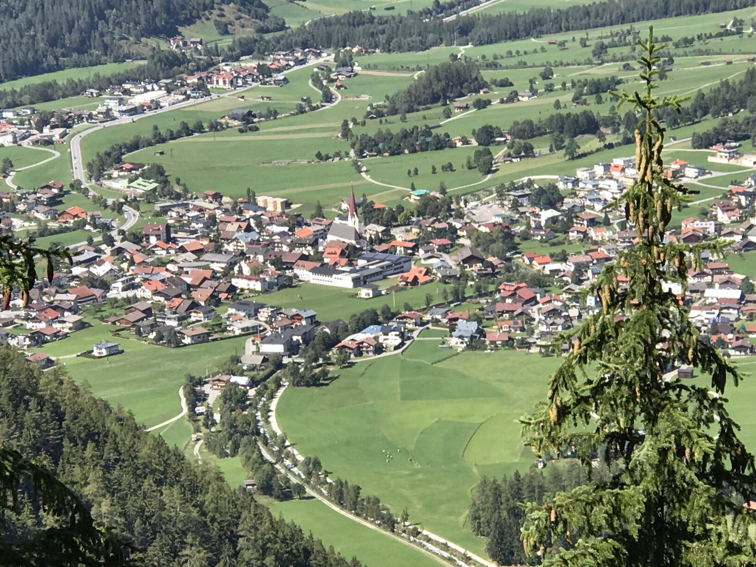 Umhausen widziane z góry w dolinie Ötztal Widok z góry na Umhausen w dolinie Ötztal, z kościołem, łąkami, drogami, domami i lasami na zboczach.
