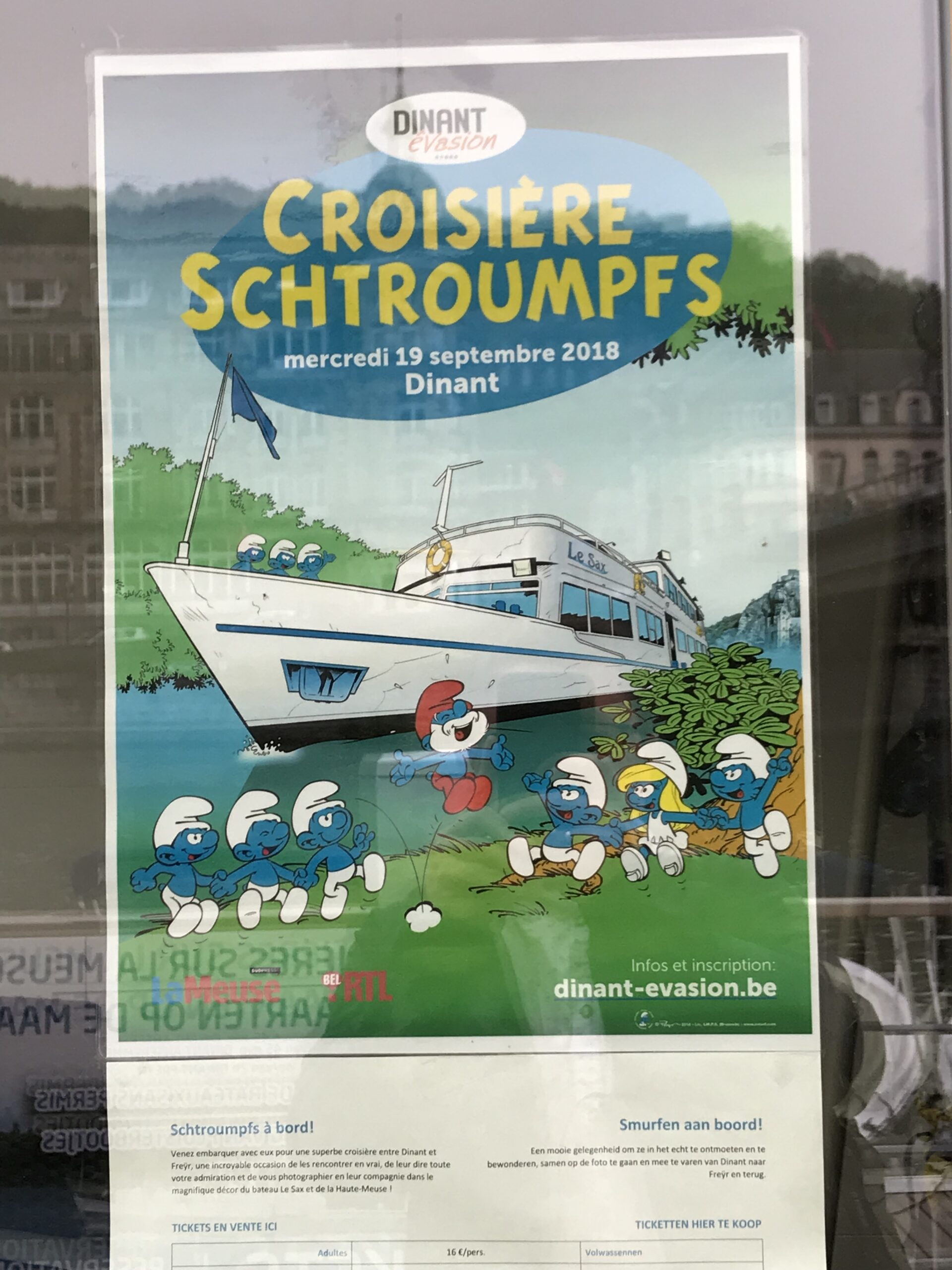Plakat rejsu Smerfów Dinant Évasion Plakat Dinant Évasion reklamujący rejs Smerfów po Mozie w Dinant, z rysunkową łodzią i postaciami Smerfów.