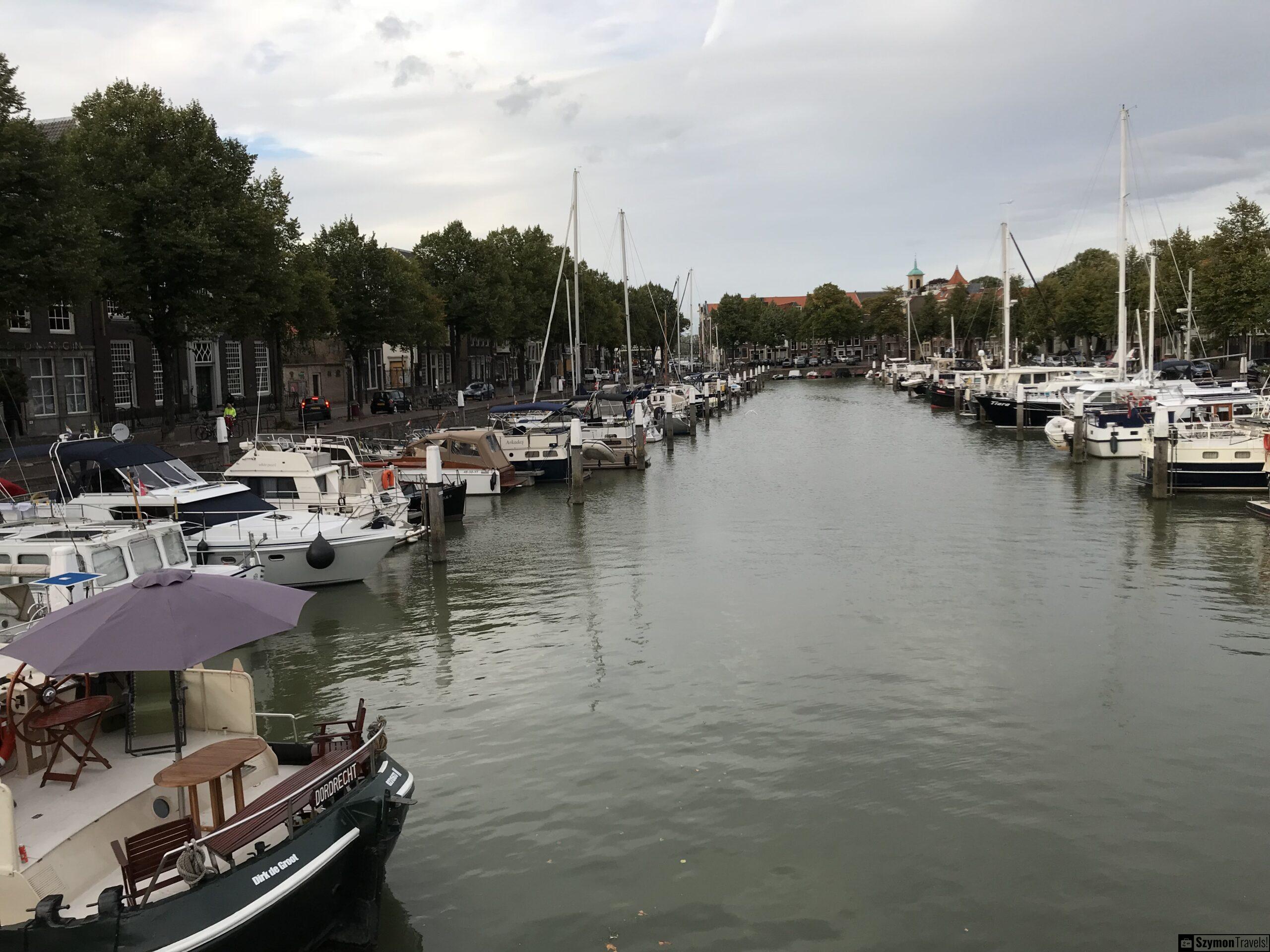 Stary port w Dordrecht z łodziami i kamienicami Szeroki widok na stary port w Dordrecht z łodziami po obu stronach wody, drzewami, kamienicami i pochmurnym niebem.