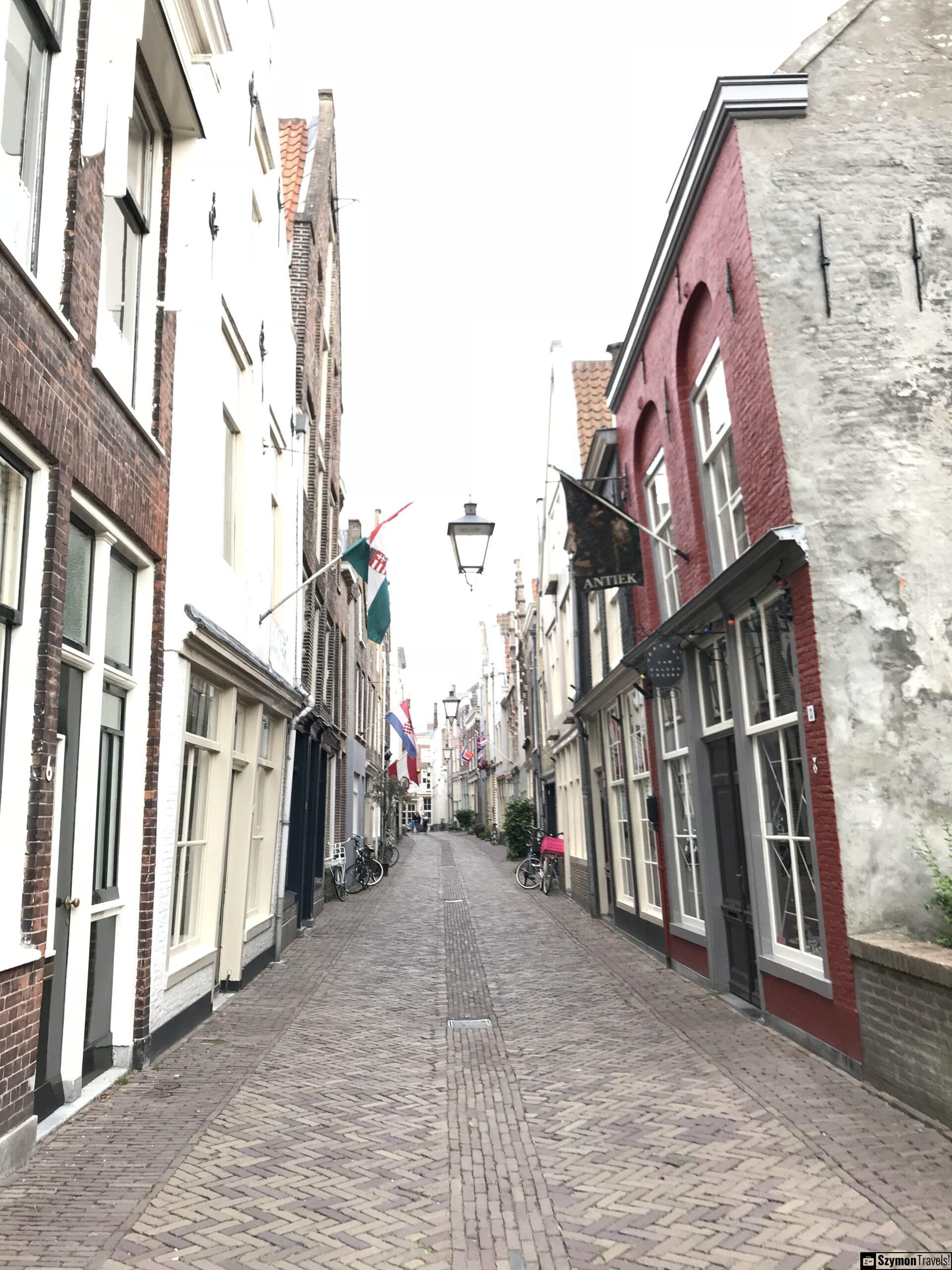 Wąska ulica w historycznym centrum Dordrecht Wąska brukowana ulica w historycznym centrum Dordrecht z ceglaną i tynkowaną zabudową, flagami, rowerami i sklepami.