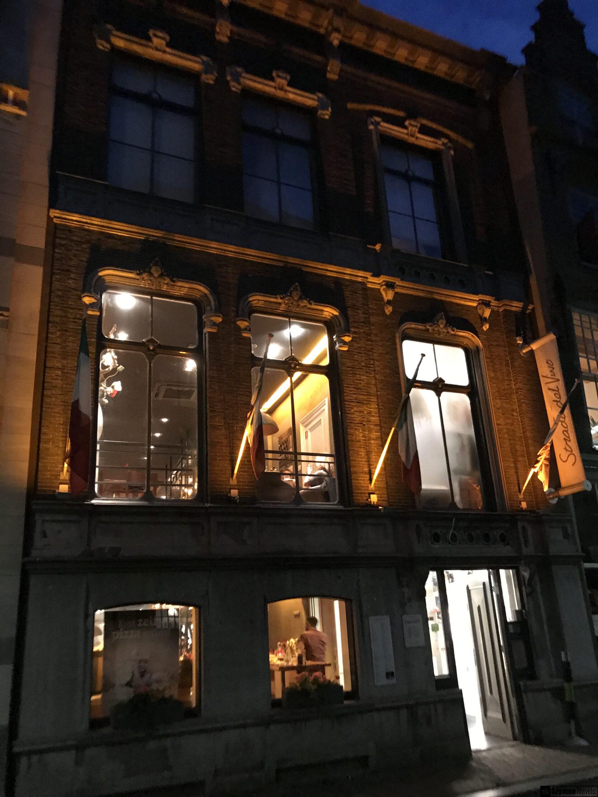 Wieczorna fasada restauracji w Dordrecht Oświetlona wieczorem fasada restauracji w Dordrecht z dużymi oknami, włoskimi flagami i ciepłym światłem wewnątrz.