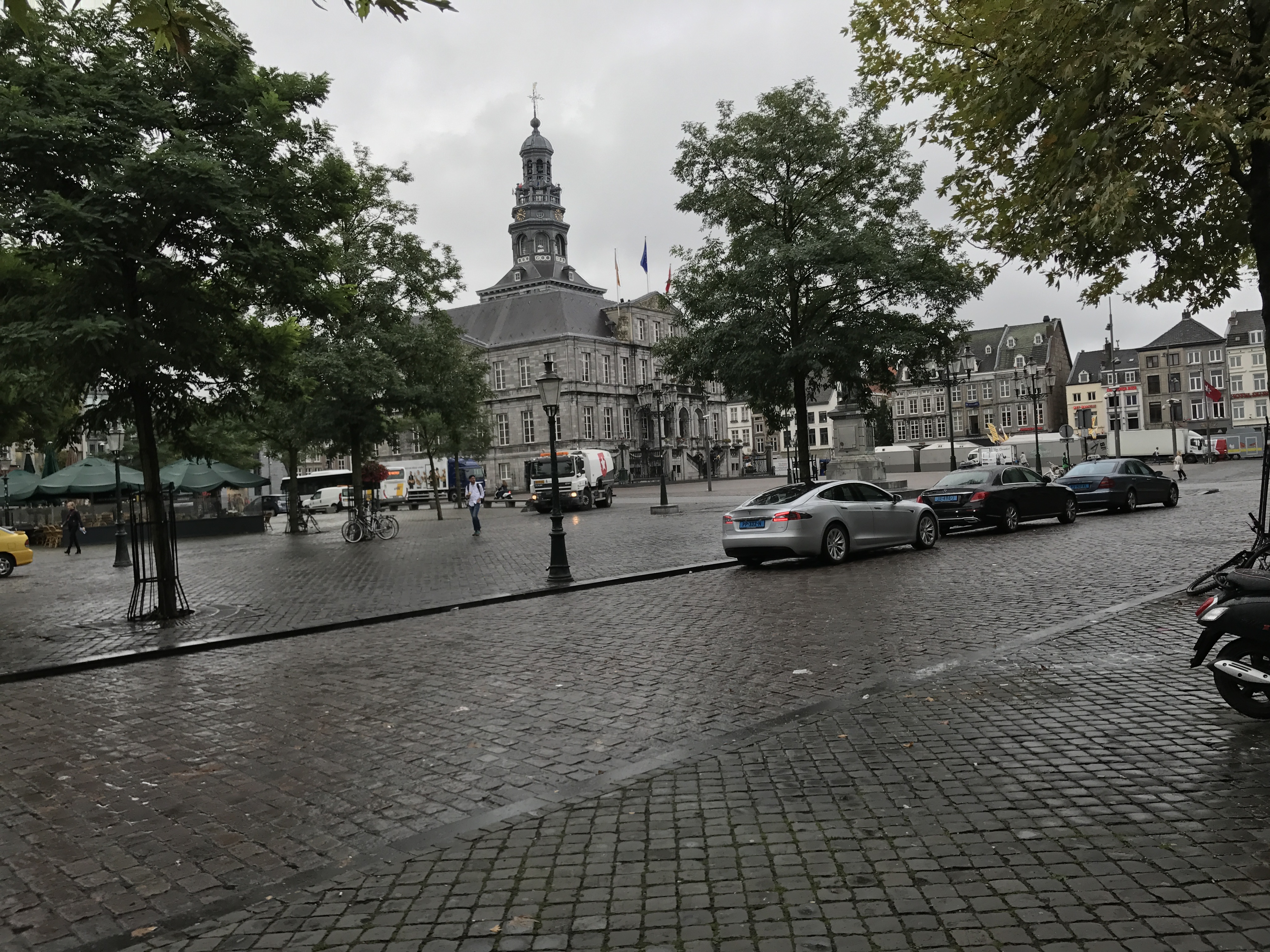 Markt w Maastricht z XVII-wiecznym ratuszem, brukowanym placem, samochodami, drzewami i pochmurnym niebem.