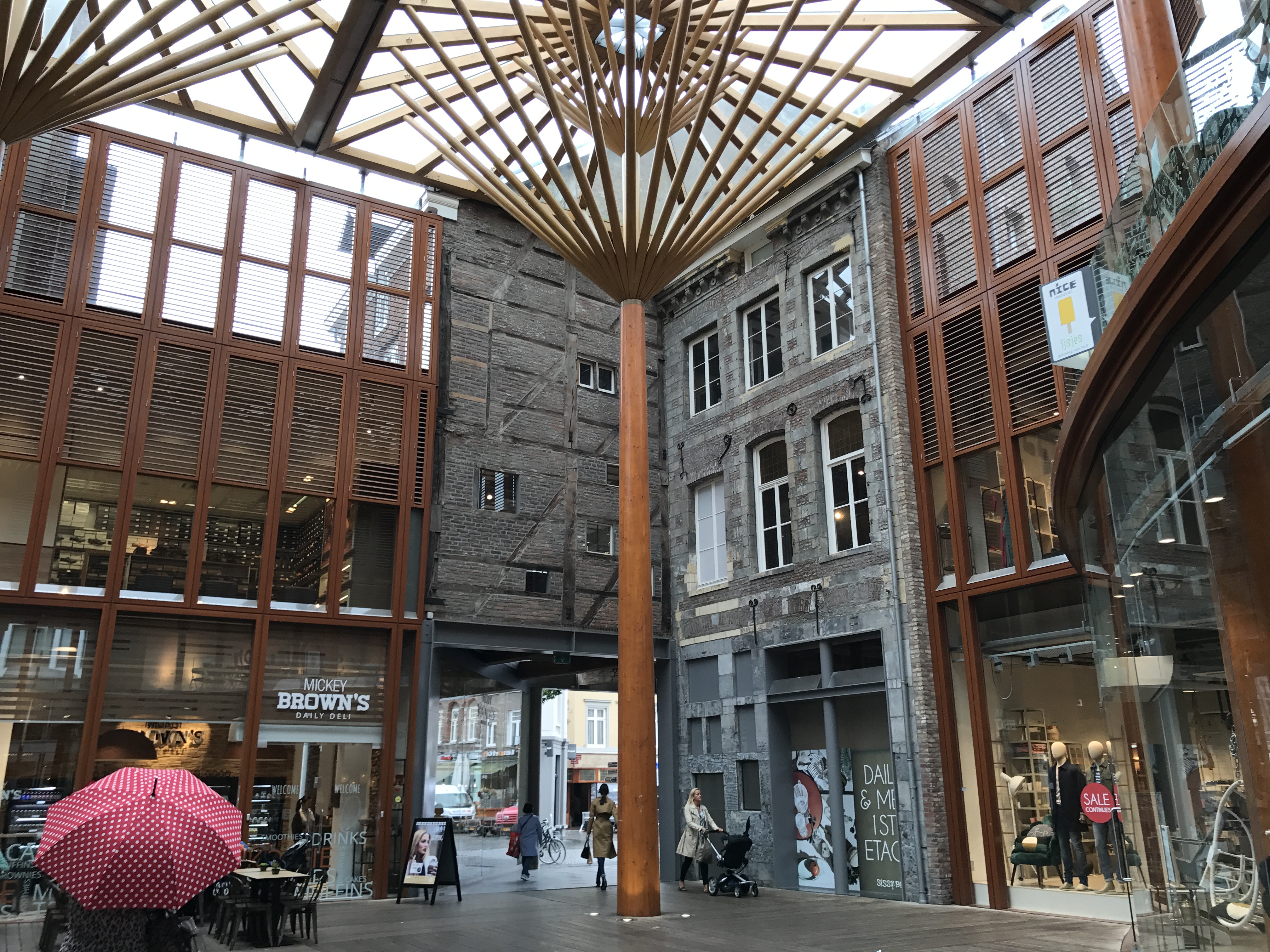 Wnętrze Mosae Forum w Maastricht z nowoczesnym drewnianym dachem, sklepami, szklanymi fasadami i przechodniami.