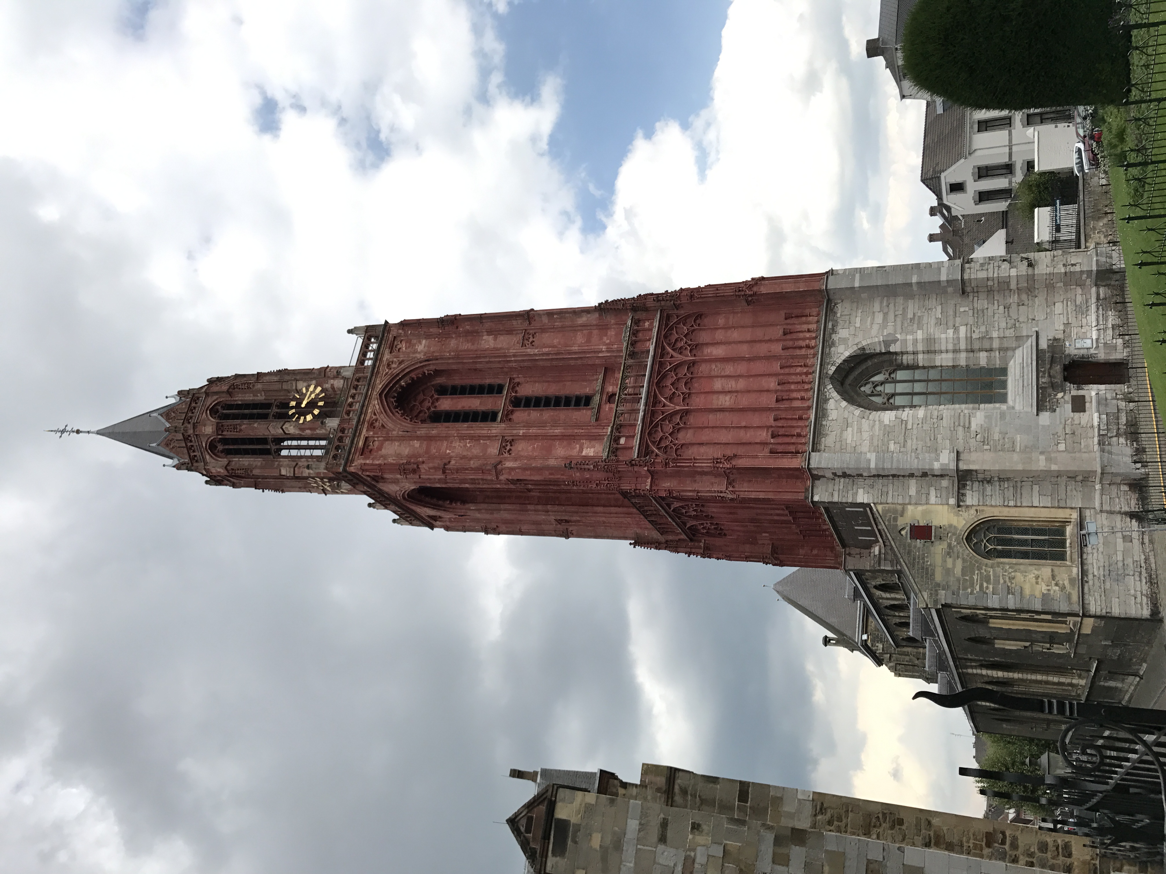 Czerwona gotycka wieża Sint-Janskerk na placu Vrijthof w Maastricht, widziana pod pochmurnym niebem.