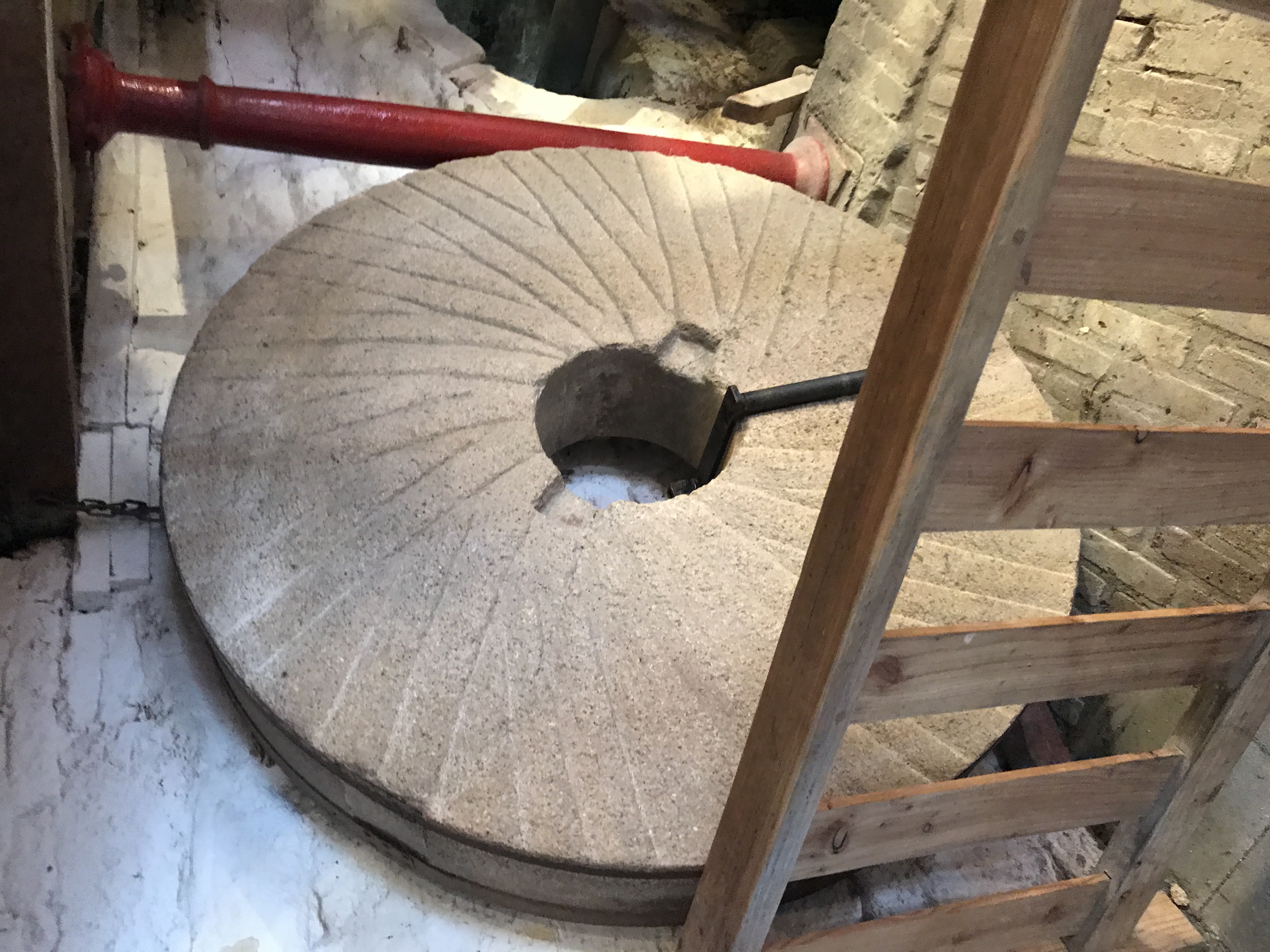Duże kamienne żarno w De Bisschopsmolen w Maastricht, widoczne za drewnianą balustradą.