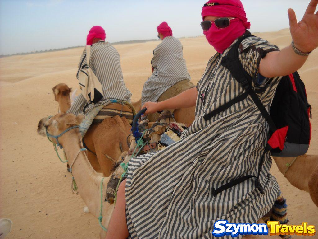 Szymon na dromaderze w pasiastej szacie i różowym turbanie na Saharze w Douz