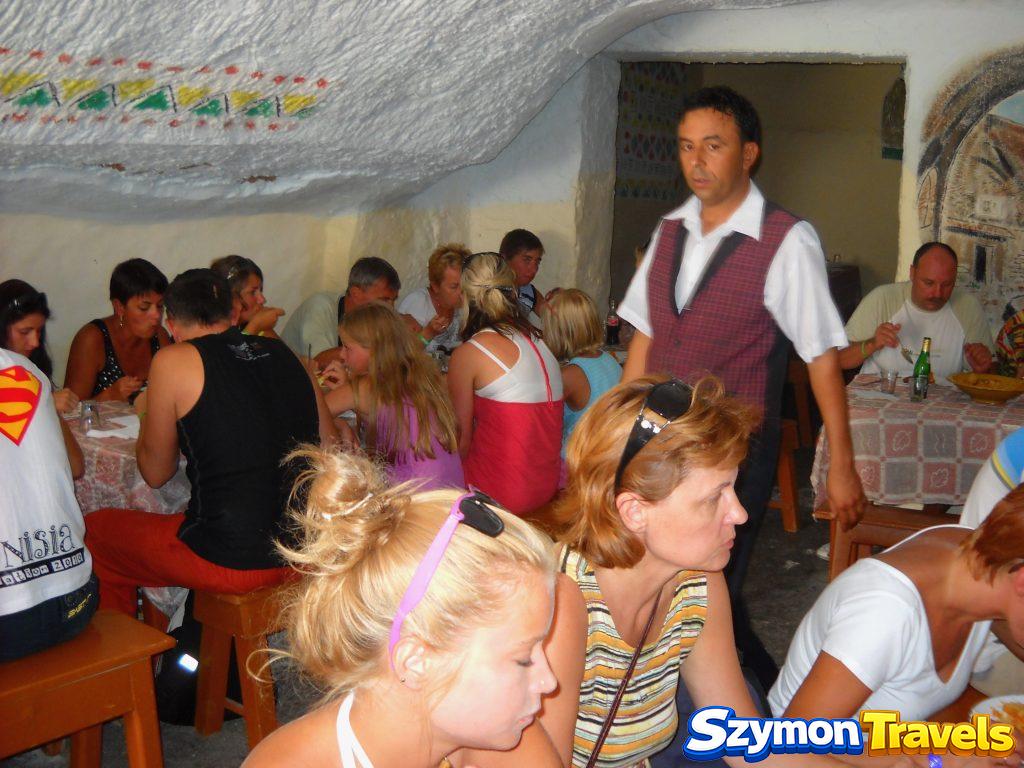 Sala obiadowa w skalnym domu troglodytycznym w Matmacie z grupą turystów przy stołach