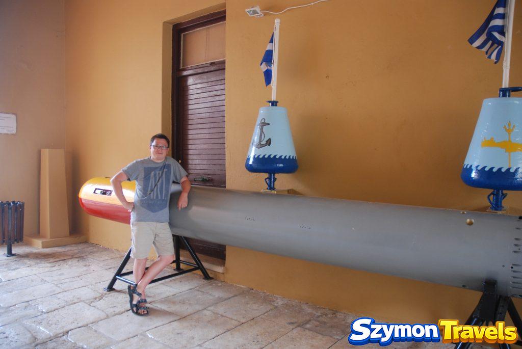 Szymon obok dużej torpedy i dekoracyjnych boi w Muzeum Morskim Krety w Chanii