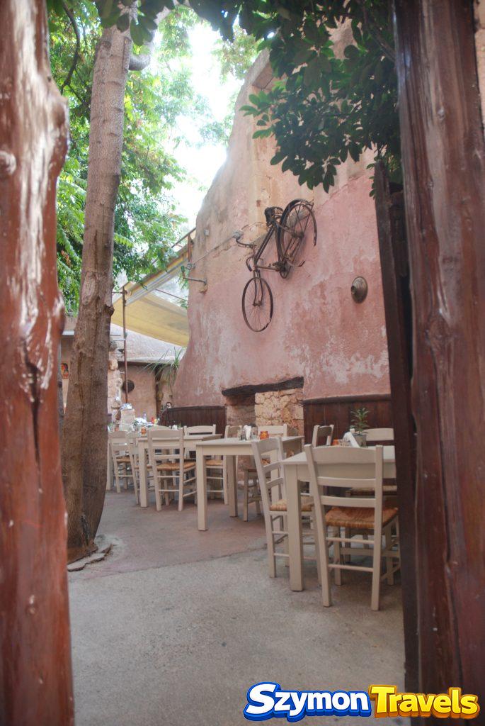 Dziedziniec restauracji w Chanii z rowerem zawieszonym na różowej ścianie