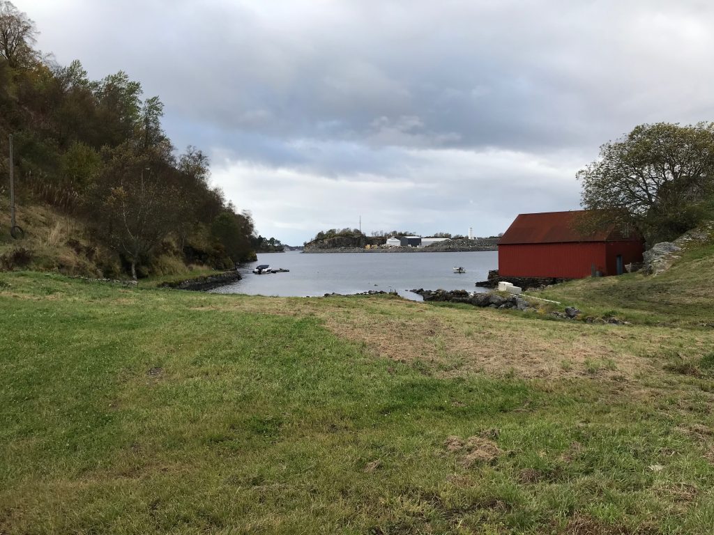 Zatoka z czerwonym domem na Askøy Zatoka na wyspie Askøy z czerwonym drewnianym budynkiem, trawą i pochmurnym niebem