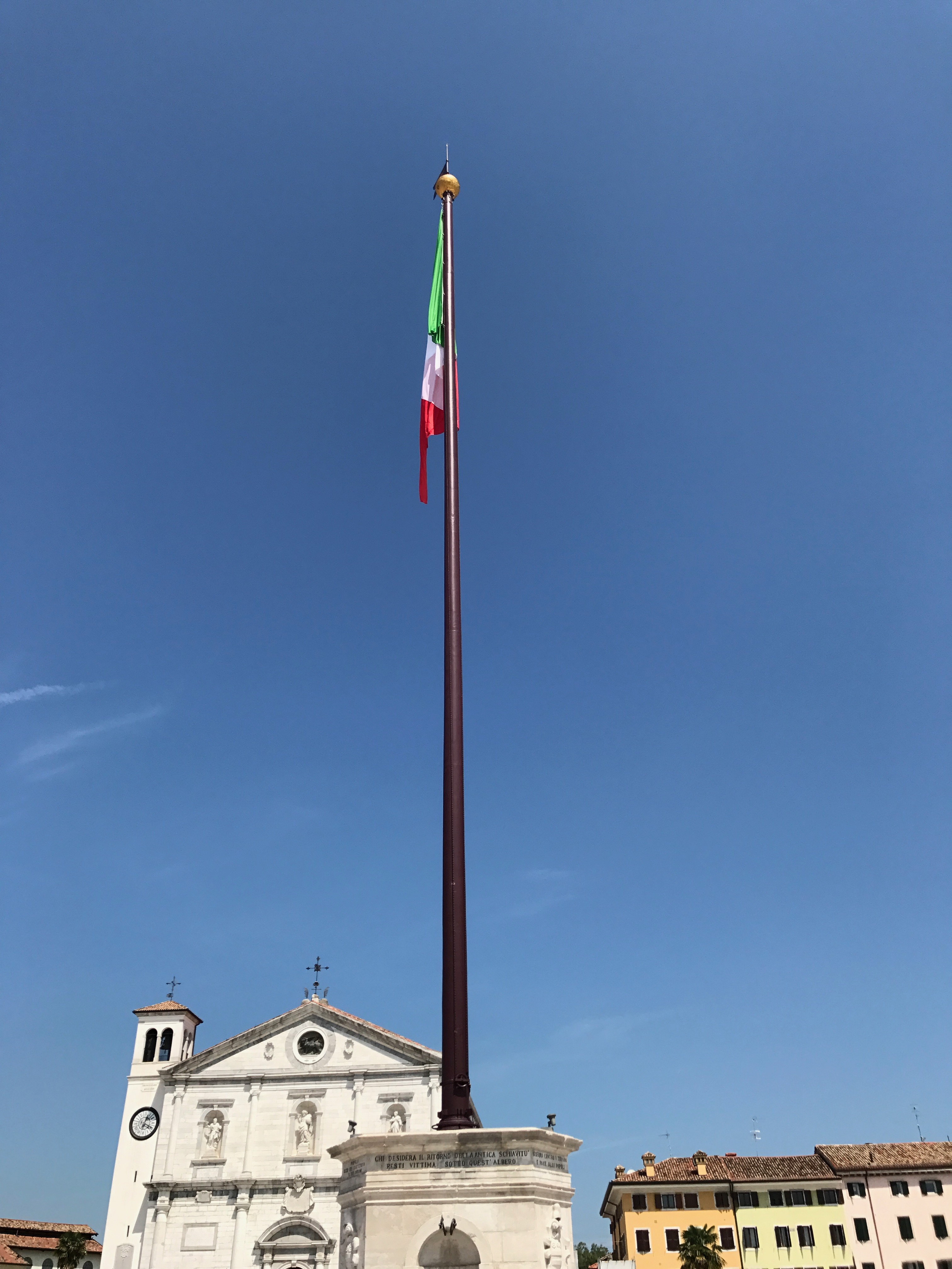 Wysoki maszt z włoską flagą na Piazza Grande w Palmanovie przed fasadą Duomo Dogale
