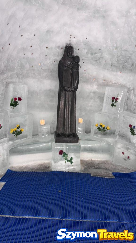 Lodowa kaplica w Glacier Palace z figurą Matki z Dzieciątkiem, świecami, kwiatami i lodowymi ławami.
