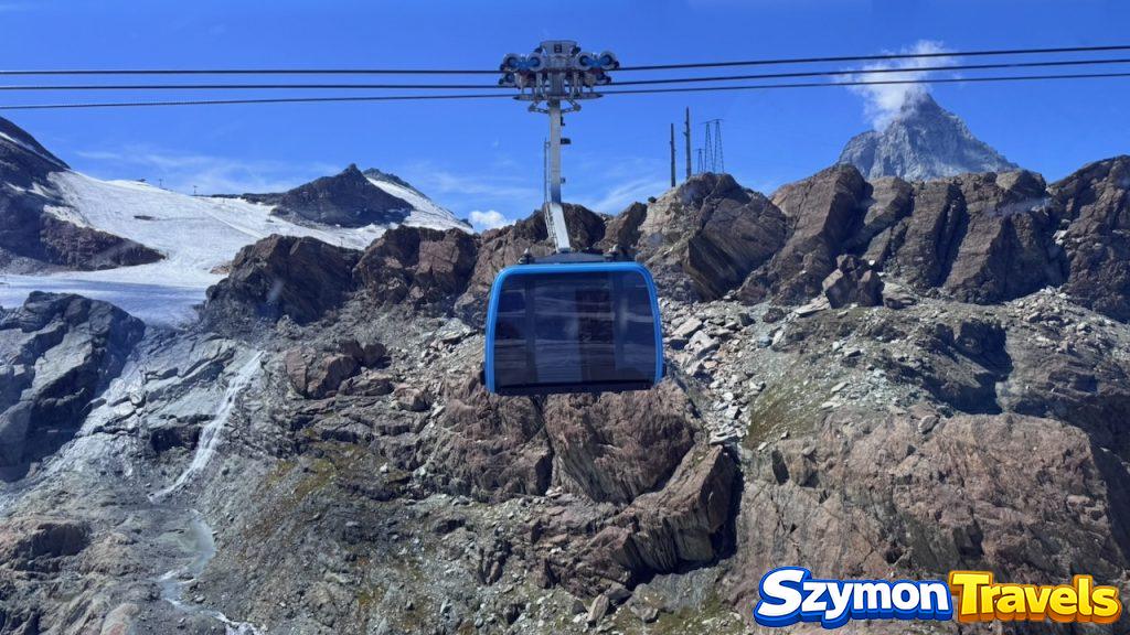 Niebieska kabina kolejki linowej nad skałami w rejonie Matterhorn Glacier Paradise, z Matterhornem w tle.