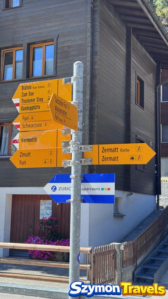 Żółte drogowskazy szlaków w Zermatt pokazujące kierunki m.in. Zermatt Kirche, Zmutt, Furi, Schwarzsee i Trockener Steg.