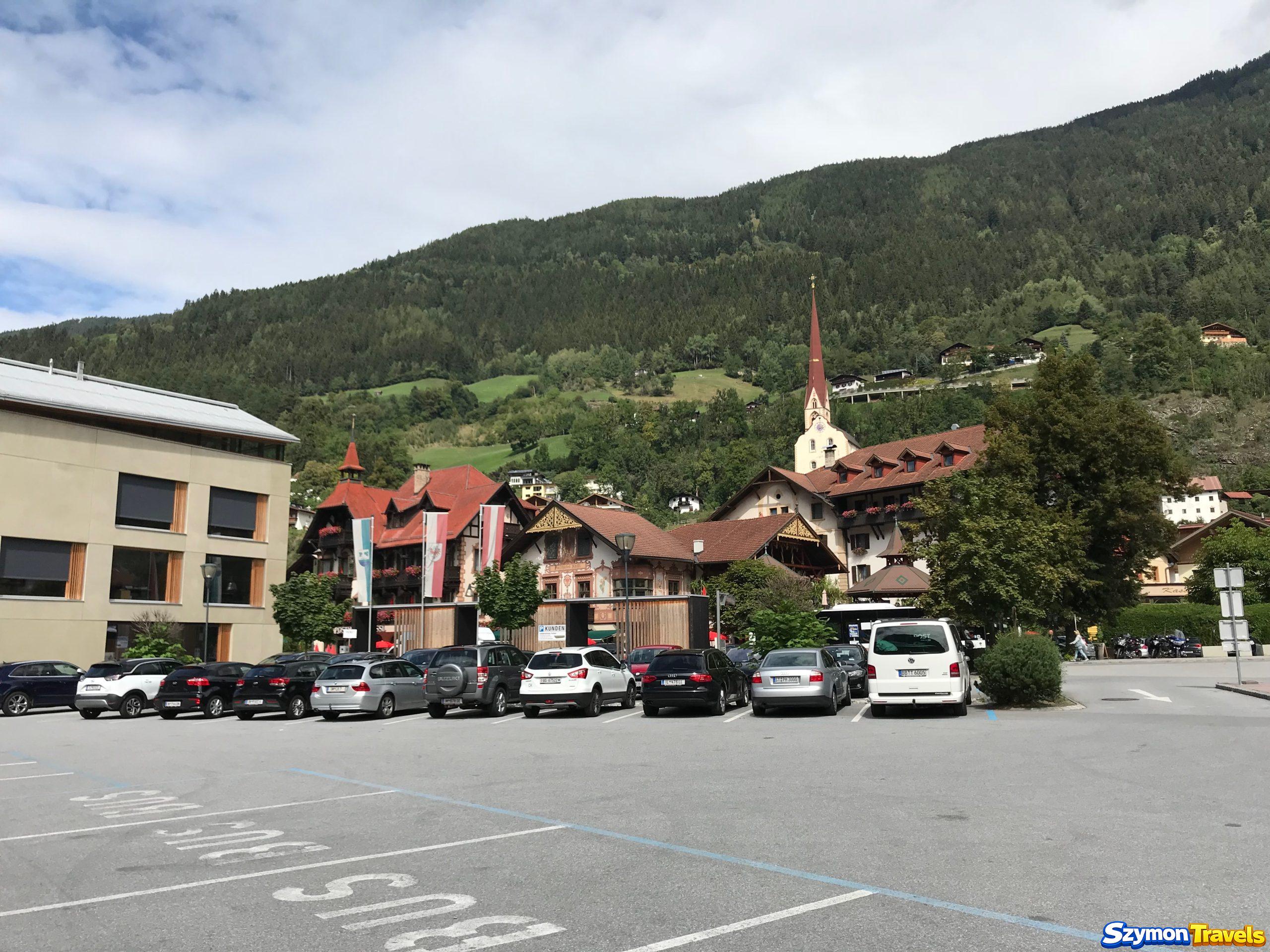 Centrum Oetz w dolinie Ötztal Centrum Oetz w Tyrolu z parkingiem, kościołem, tradycyjnymi budynkami i zielonymi zboczami gór nad miejscowością.