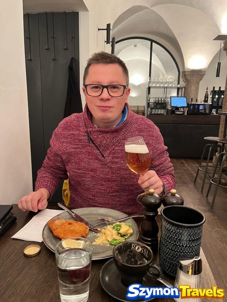 Szymon z piwem podczas kolacji w Innsbrucku Szymon siedzący przy stole w restauracji w Innsbrucku, trzymający kielich piwa; przed nim stoi talerz z obiadem.