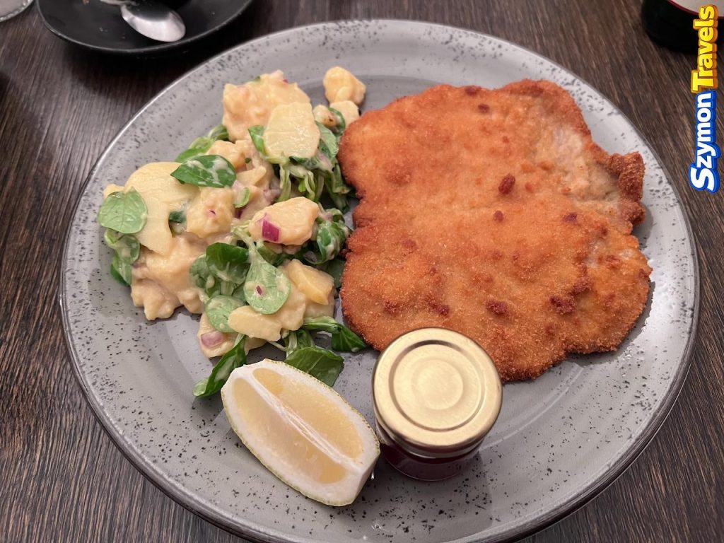 Panierowany sznycel podany z sałatką ziemniaczaną, roszponką, cytryną i owocowym dodatkiem w restauracji w Innsbrucku.