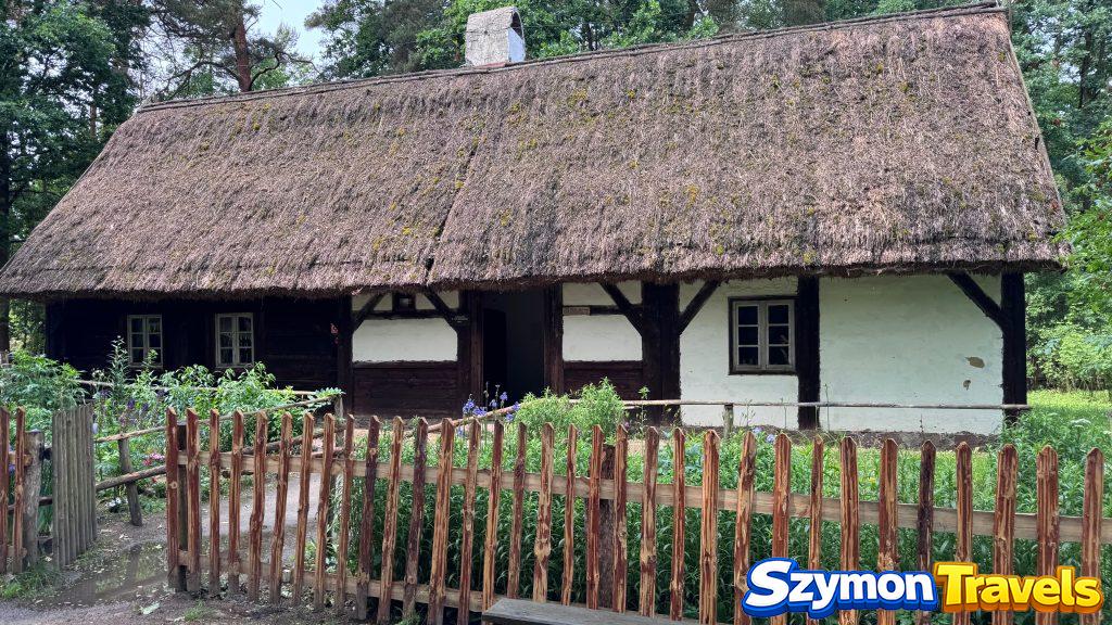 Drewniana chałupa kryta strzechą z płotem i ogródkiem w Muzeum Etnograficznym w Ochli