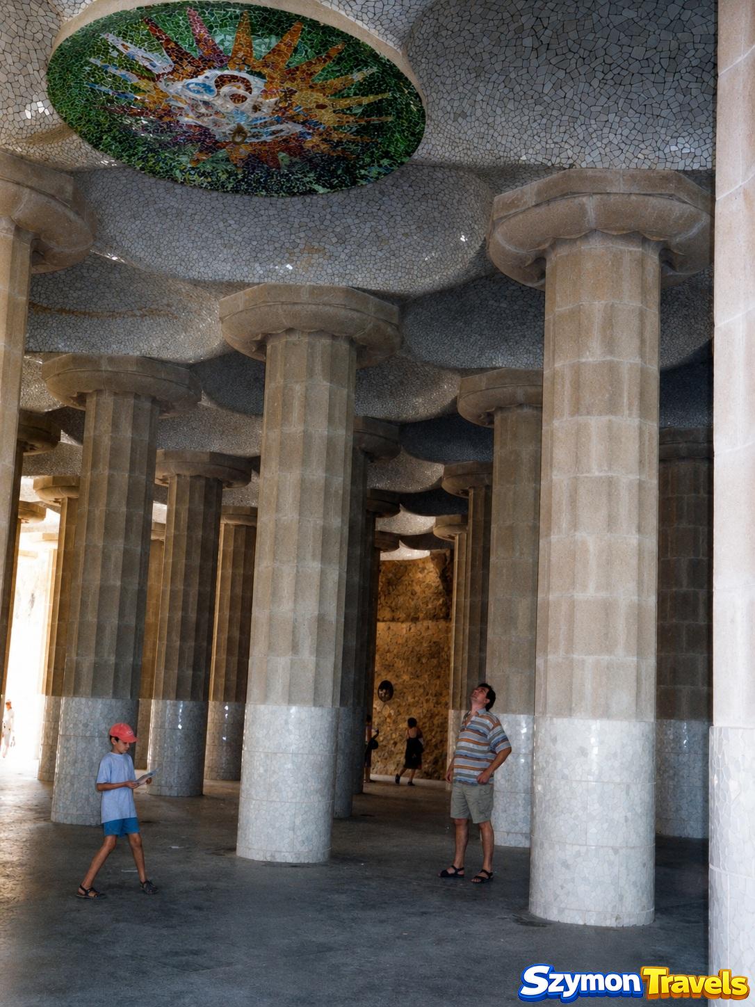 Wnętrze Sali Hipostylowej w Park Güell z kamiennymi kolumnami i kolorową mozaikową rozetą na suficie