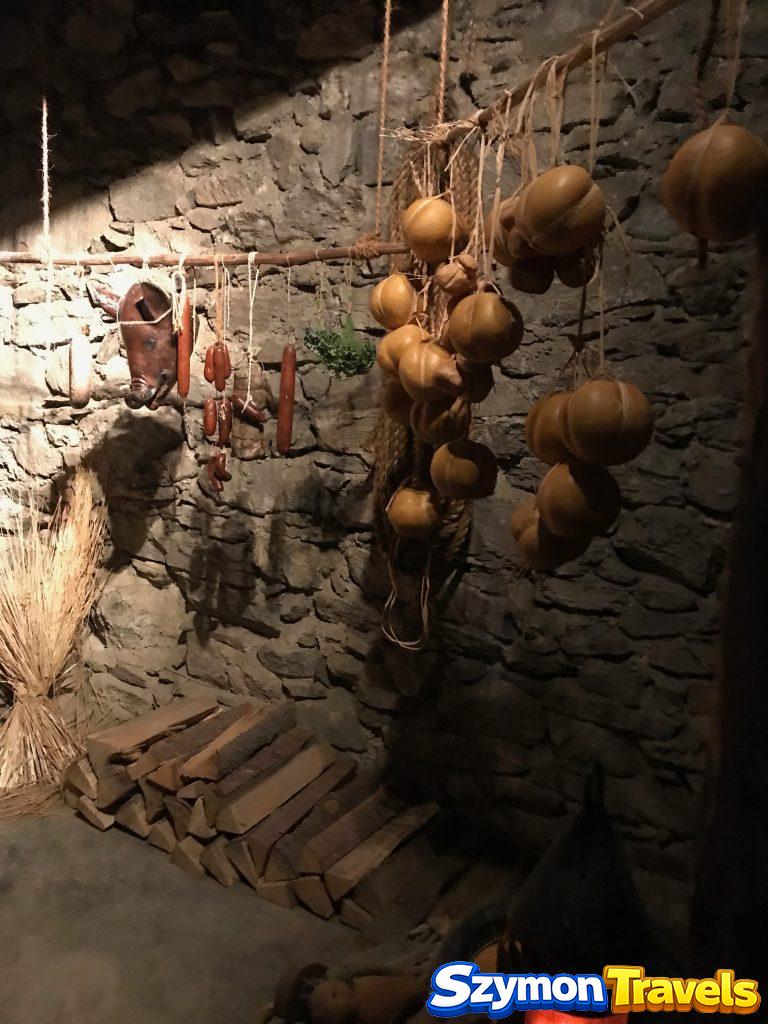 Schloss Moosham – ekspozycja dawnej spiżarni Muzealna ekspozycja dawnej spiżarni w Schloss Moosham z wiszącymi wędlinami, serami, zbożem i drewnem opałowym