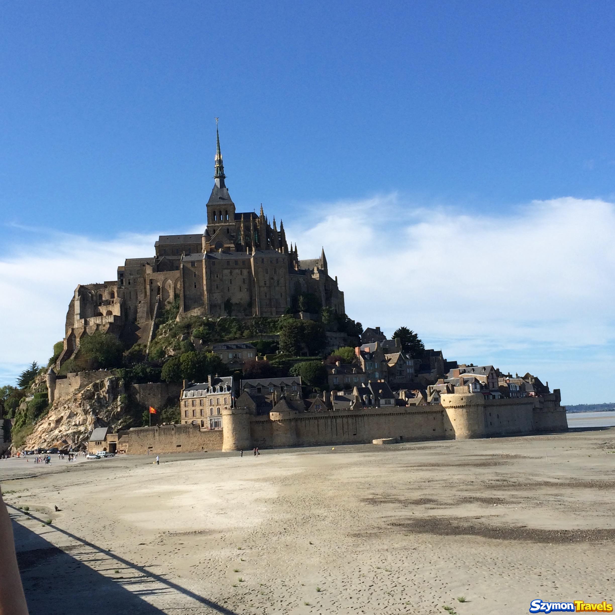 Mont-Saint-Michel podczas odpływu, z opactwem, murami i średniowieczną zabudową u podnóża skały