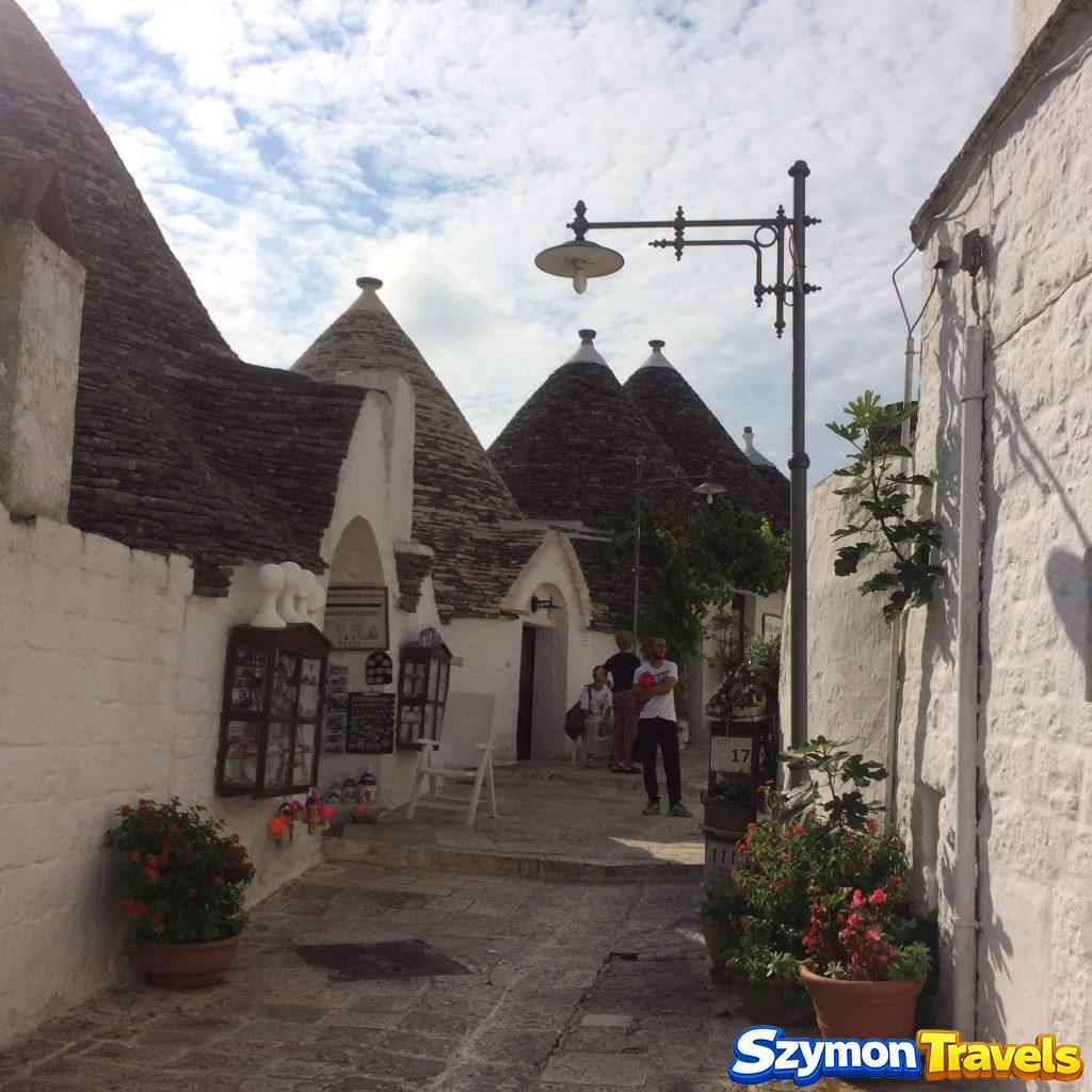 Kamienna uliczka w Alberobello z białymi domami trulli, kwiatami i małymi sklepikami