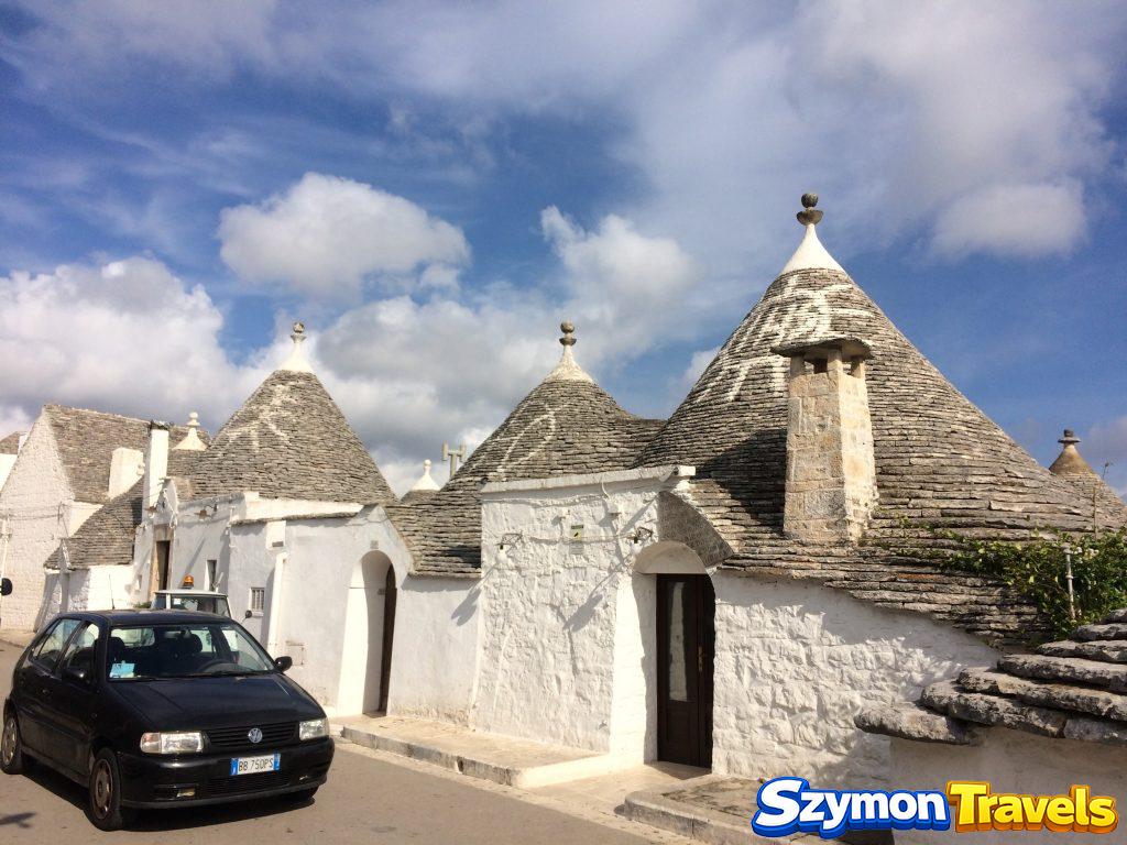 Białe domy trulli z kamiennymi stożkowymi dachami przy ulicy w Alberobello, z zaparkowanym samochodem
