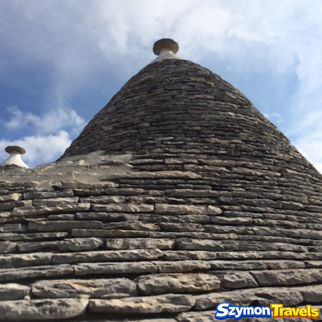 Stożkowy dach trullo z kamiennym pinaklem na tle nieba w Alberobello