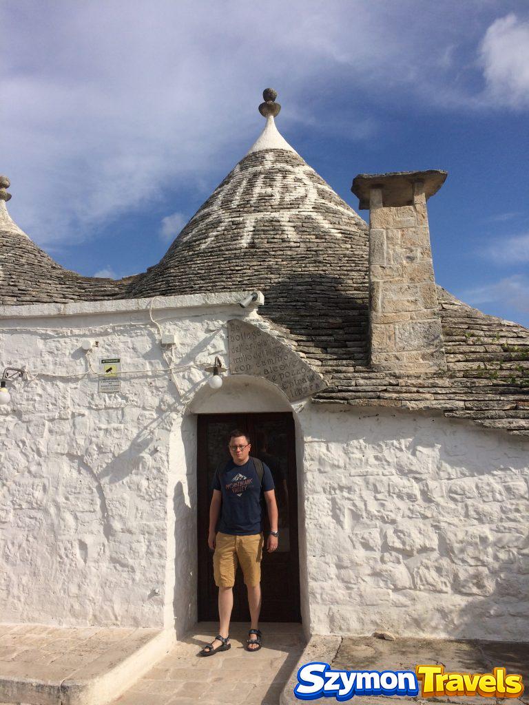 Szymon przed bielonym domem trullo ze stożkowym dachem w Rione Monti w Alberobello