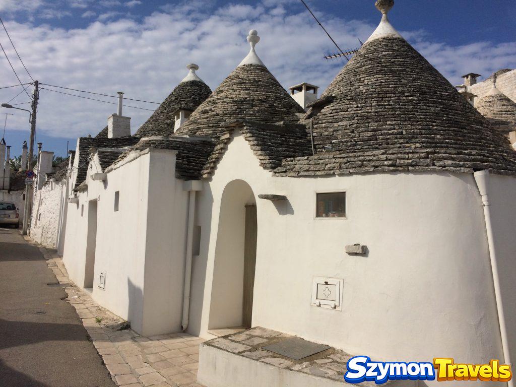 Zespół białych trulli o kilku stożkowych dachach przy ulicy w Alberobello