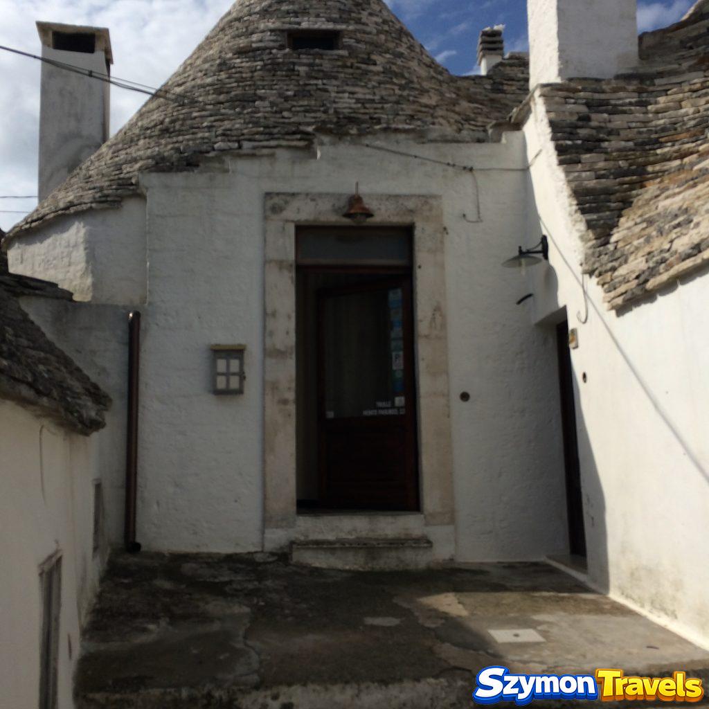 Wejście do trullo otoczone białymi ścianami, kamiennymi dachami i kominami w Alberobello