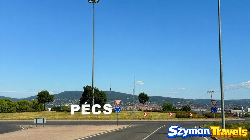 Napis Pécs przy wjeździe do miasta i wzgórza w tle