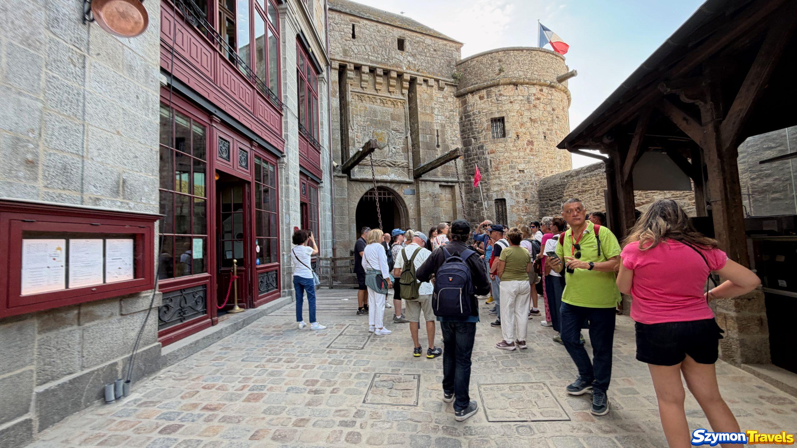 Tłumy przy wejściu do Mont-Saint-Michel Tłum przed średniowieczną bramą Mont-Saint-Michel rano w sierpniu 2026 roku