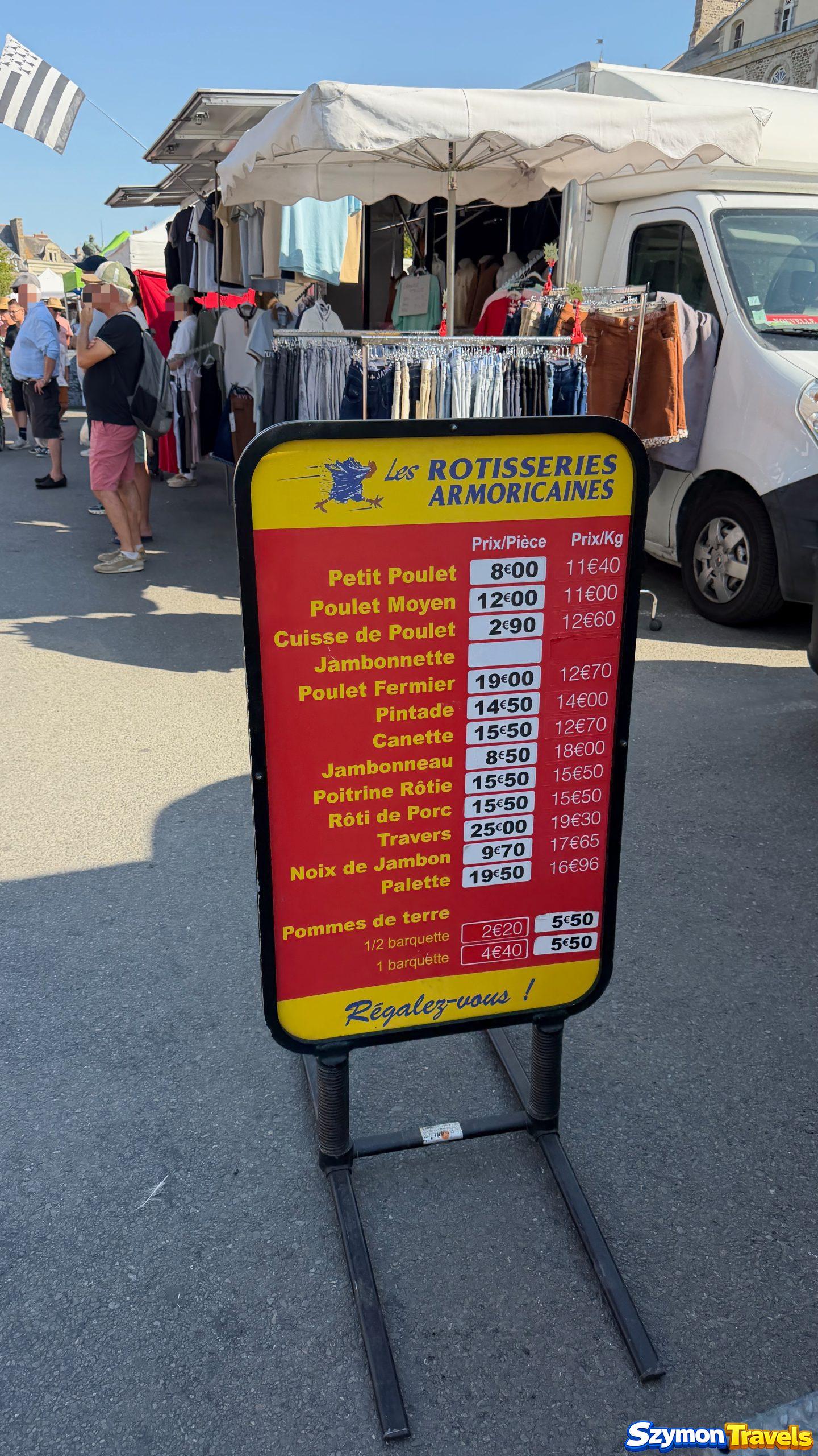 Cennik rotisserie na targu w Dinan oraz stoiska odzieżowe w tle